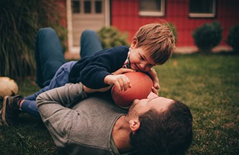 Son laying on Dad in grass with football