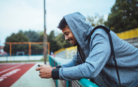Handsome young African sportsman wearing hood holding his cell phone and smiling.