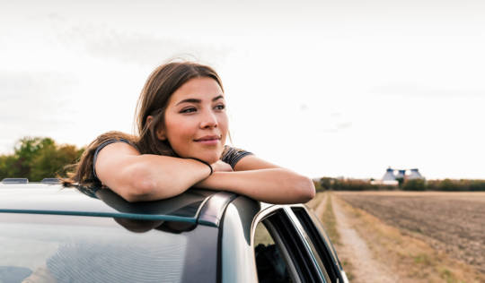 Smiling young woman looking out of sunroof of a car